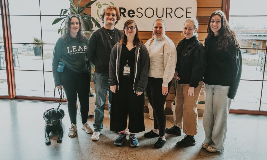 LEAP trainees and staff smile in a row inside a building, with a black dog sitting at the left.