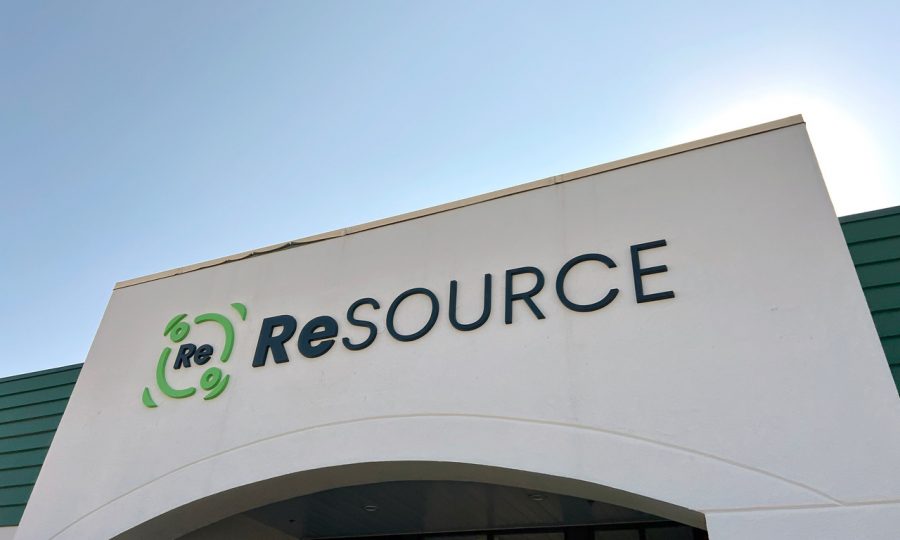 ReSOURCE Morrisville building with a sign that reads "ReSOURCE" in green and black letters is prominently located under a clear blue sky. The logo, featuring a circle with arrows around "Re," marks the store's eco-friendly focus.