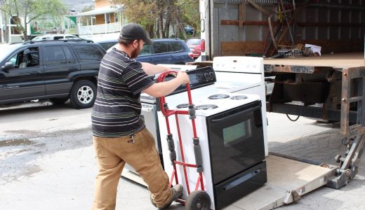 ReSOURCE employee with a cap loading a white stove onto a red dolly, preparing for donation pick-up, reflecting ReSOURCE's mission of environmental stewardship through recycling household goods.