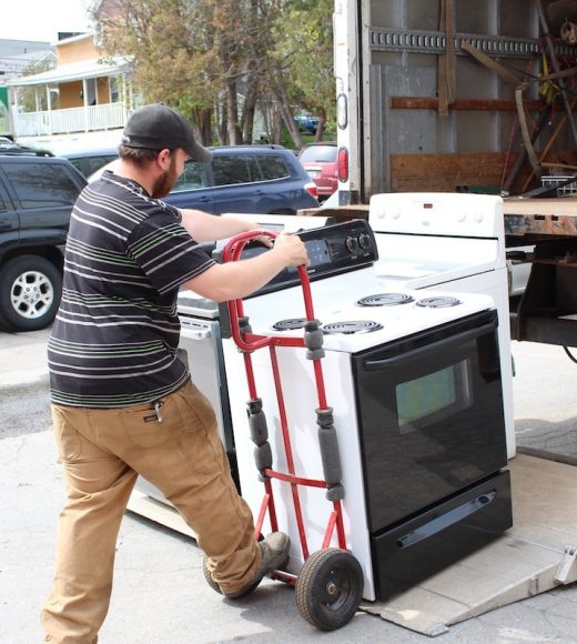 ReSOURCE employee with a cap loading a white stove onto a red dolly, preparing for donation pick-up, reflecting ReSOURCE's mission of environmental stewardship through recycling household goods.