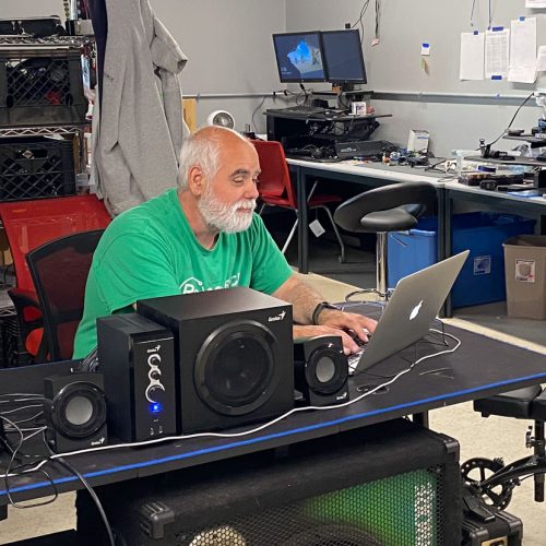 Dedicated technician at ReSOURCE Vermont's repair shop providing computer sales and services, surrounded by electronics and repair tools, accessible to all Vermonters.